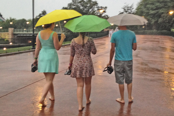 Three people walking in Disney in the rain with umbrellas