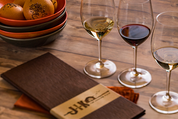 Three glasses of wine on wooden table next to Jiko drink menu