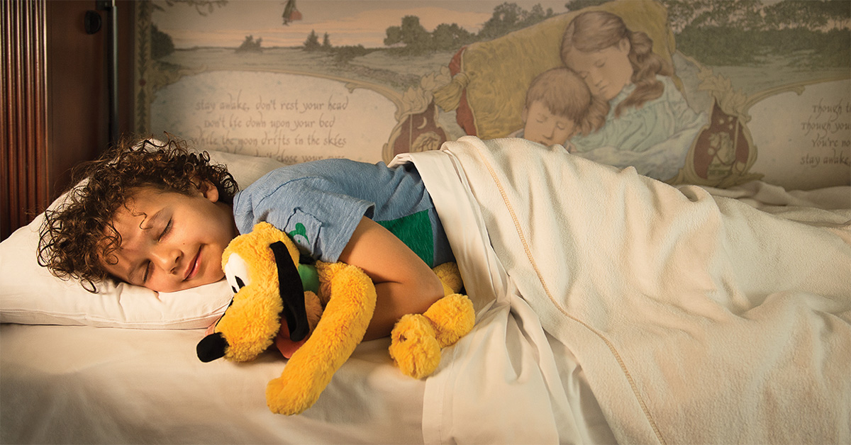 child with Pluto stuffed animal sleeping on pull down bed in Disney hotel