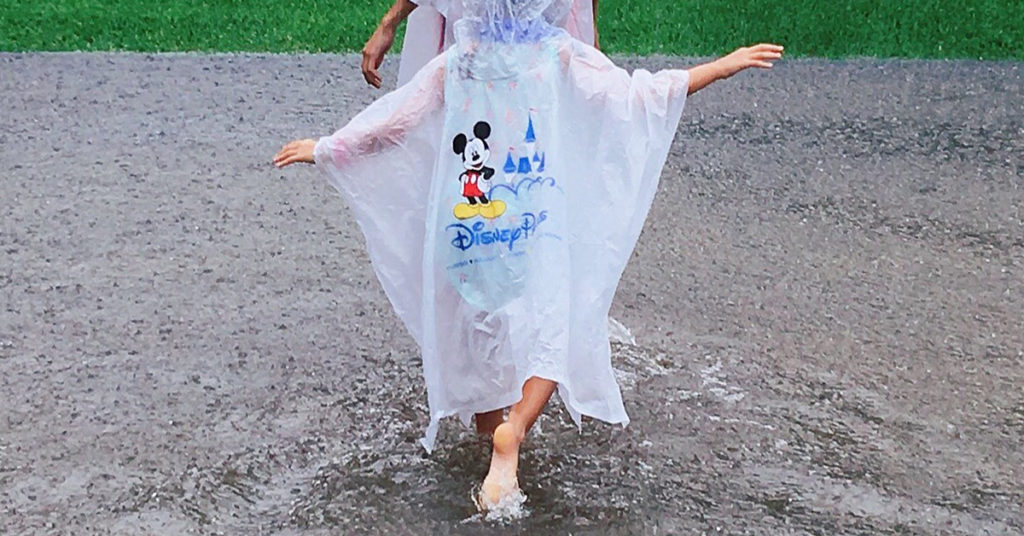 child running barefoot in the rain wearing a Disney poncho