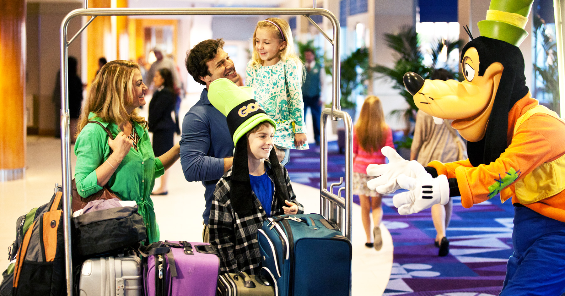 family of four with luggage on luggage cart checking into hotel and being greeted by Goofey